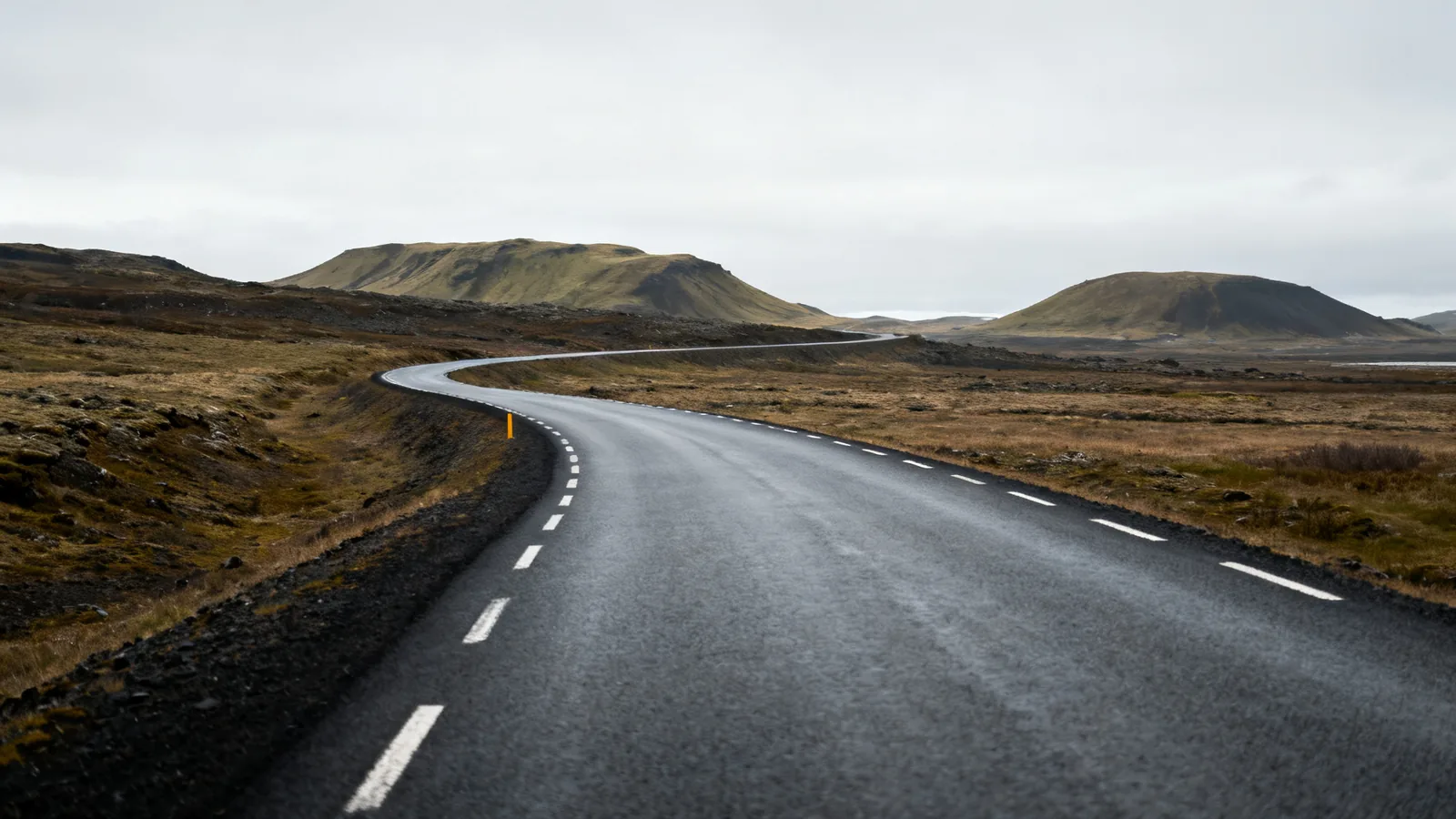Anonymous paved rural road curving toward low Icelandic hills