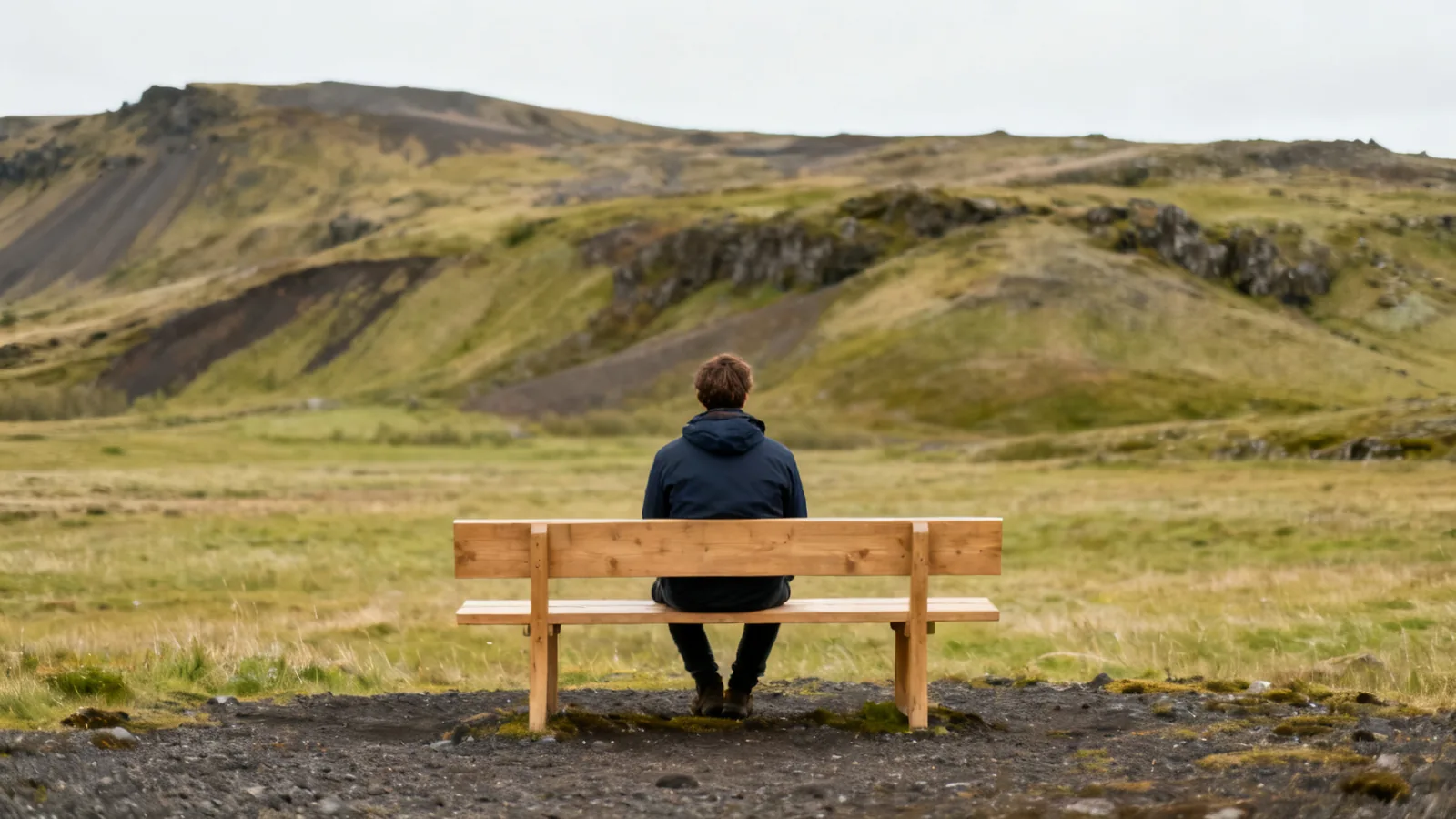 Distant traveller seated on a bench overlooking anonymous Icelandic hills